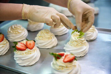 Person topping a dessert with strawberries and whipped cream