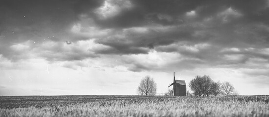 classical black and white panoramic landscape of farmland with old wooden windmill under dramatic sky