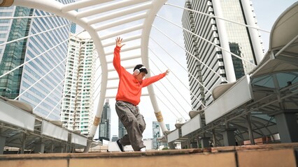 Asian hipster wearing headphone show footstep while jumping at city. Professional break dancer...