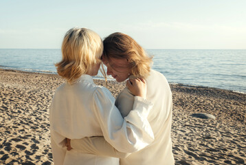 Mom and daughter are standing on the beach by the sea, hugging