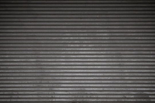 Front view of an old and weathered closed security roller door (or roller shutter, sectional overhead door, roll up or rolling garage door). Abstract full frame garage door background in black & white