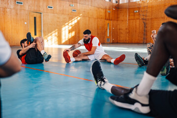 Basketball player stretching his legs while sitting on a floor in a sports hall