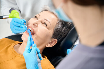 Nurse holds saliva ejector while dentist engaging in professional tooth cleaning