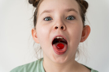 Funny little girl holding a pill on her tongue. A lollipop on the tongue of a little girl. Selected focus.