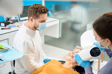 Dental assistant holding portable dental x-ray to make image of clients teeth