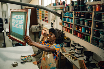 Interracial smiling female workers looking at silk screen printing plate