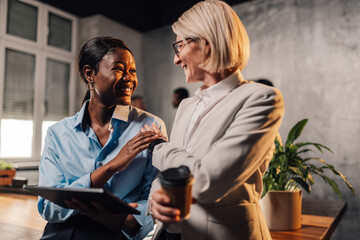 Interracial businesswomen discussing project on a tablet at workspace.