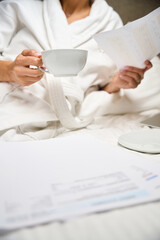 Partial businesswoman wearing bathrobe with cup watching document on bed