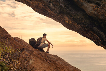 Young male hiker traveler siting on mountain top enjoying the beautiful ocean sunrise 