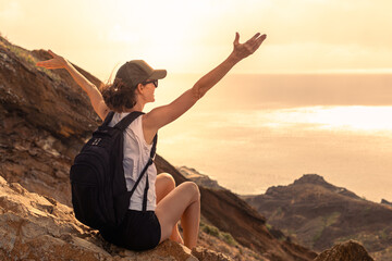Young female traveler feeling grateful, happy having joyful  mindset  sitting looking out at summer Mountain view at sunset and enjoying peace in nature
 - obrazy, fototapety, plakaty