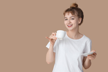 Portrait of pretty young woman in pajamas with cup of coffee on beige background