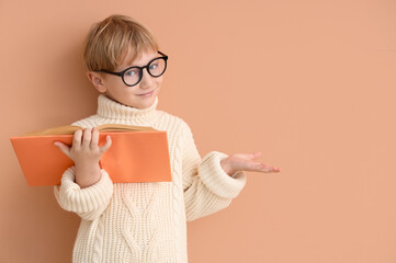 Cute little boy in eyeglasses with open book showing something against color wall