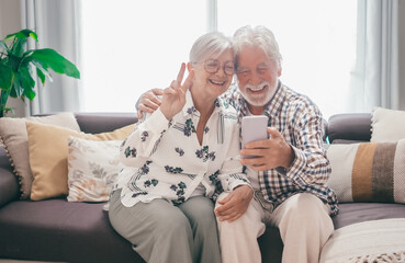 Video call concept. Happy smiling senior family couple sitting on sofa using mobile phone webcam to...