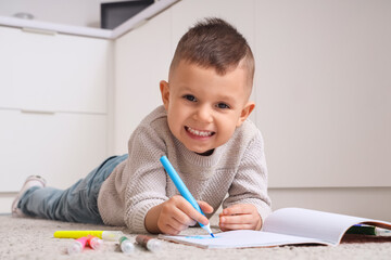Funny little boy drawing with felt-tip pens on floor in kitchen