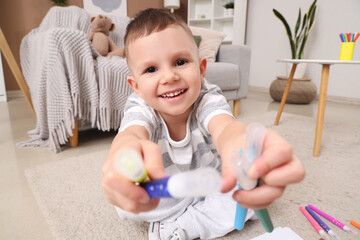 Cute little boy with felt-tip pens sitting on floor at home, closeup