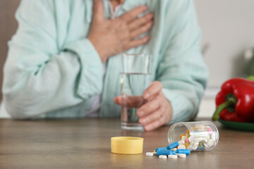 Overturned pill bottle on table of senior woman in kitchen, closeup