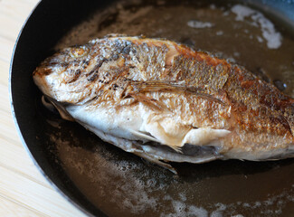 Complete gilthead sea bream fried in frying pan in butter
