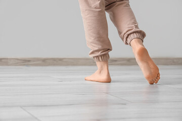 Barefoot woman walking on laminate floor in light room, back view