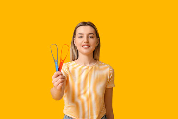 Young woman with tongue scrapers on yellow background