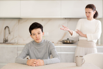 Portrait of offended teenager sitting at home while mother berating him