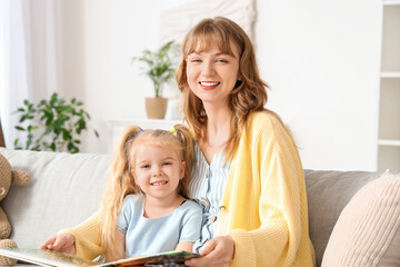 Nanny reading story to little girl on sofa at home