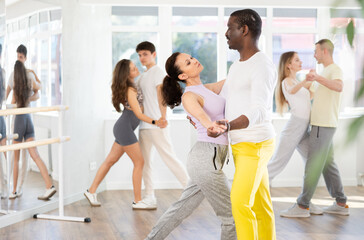 Smiling young woman wearing sportswear dancing in couple rumba dance with african american partner...