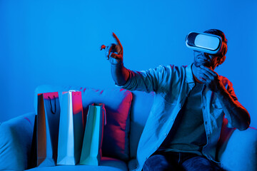 Caucasian man with vr glass posing pointing finger while sitting at sofa with shopping bags. Person...