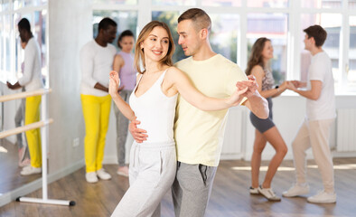 Positive woman and man dancing bachata in pair during group dance classin dancing studio