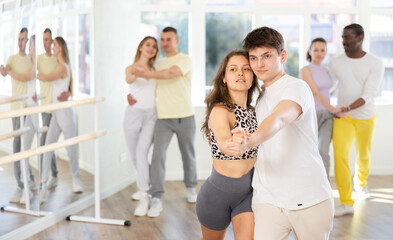 Slim young man and woman practicing waltz dance in training hall during group dancing classes