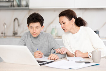 Boy and his mother study via video conference using a laptop in kitchen