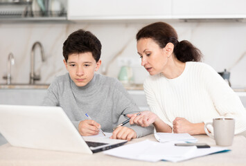 Fototapeta premium Boy and his mother study via video conference using a laptop in kitchen