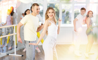 Slim young man and woman practicing active dance in training hall during group dancing classes