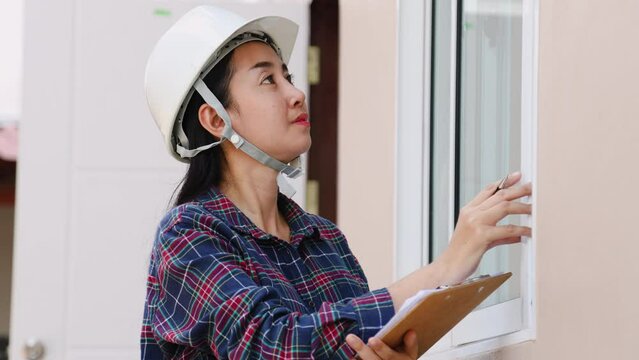 Portrait of Asian woman inspector worker wearing white hardhat notes and measuring wooden door on real estate or townhouse construction sites, house inspection specialist career for female occupation