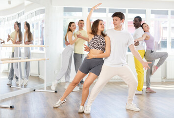 Fototapeta premium Positive guy dancing playful Latin dance bachata with attractive young female partner during group class in choreography studio..