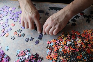 Close-up of adult caucasian hands diligently putting together a vibrant and intricate jigsaw puzzle...