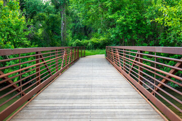 Fototapeta premium A rustic wooden bridge, adorned with rust-colored railings, beckons entry into a wooded forest sanctuary adorned with thick foliage.