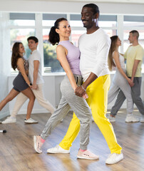 Beautiful young woman at modern dance salon with her african american partner dancing tango