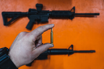 Shooting weapons in a shooting range. A 5.56x45mm cartridge in a man's hand and an m4a1 rifle on an...