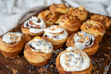 Freshly baked cinnamon rolls with white icing and silver sugar beads on a wooden board, hinting at a festive occasion.