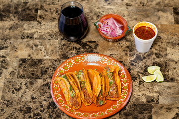 high view of four birria tacos on a clay plate with consome, onion, and limes traditional Mexican food