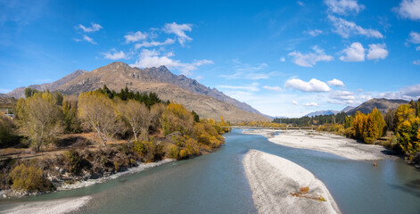 Panorama view of a freshwater river with clear, blue shallow water flowing through a mountainous area in a valley. Beautiful nature landscape overlooking Shotover River, Queenstown New Zealand.