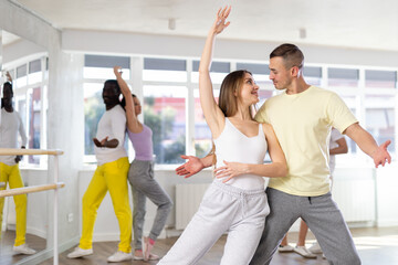 Positive young adult woman learning to dance tango with male partner in choreography class,...