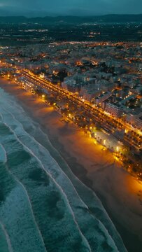 illuminated streets of Spanish touristic city Salou, Catalonia, aerial view of beach, sea and coast with palm trees, aerial drone view 4k, vertical video