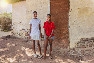 two smiling african teenager girls in front of the house in the poor township, informal settlement