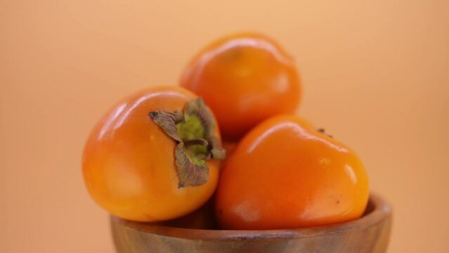 Circular motion: beautiful ripe persimmon in a wooden plate on a brown background.