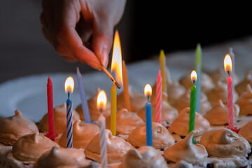 Hand holding matches and lighting colorful candles on the large homemade chocolate birthday cake,...