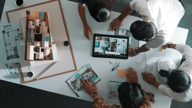 Time lapse of designer looking at model while discussing about building. Top view of architect engineer explaining idea while talking and writing blue print scattering at meeting table. Alimentation.
