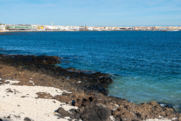 Fototapeta na wymiar Walking on sea promenade in Corralejo along white popcorn beach with white corals, black rocks, blue water, Fuerteventura, Canary islands, Spain