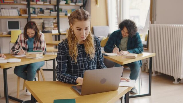 a group of students study and read books, write information in notebooks, on their phones and laptop in a library or classroom. Students in a good mood studying and reading books in the library