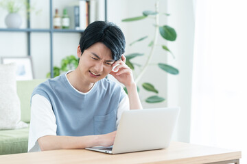 リビングでパソコンを使って悩む若い日本人の男性